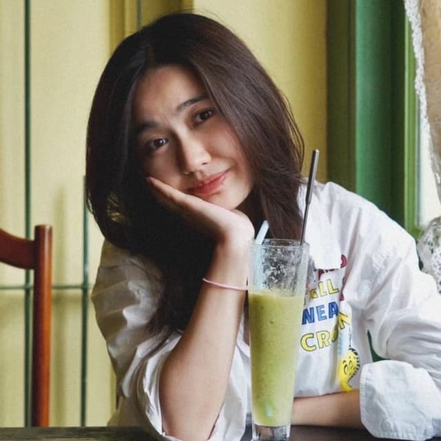 Headshot of a Chinese lady wearing a white shirt, with a matcha drink in front of her.